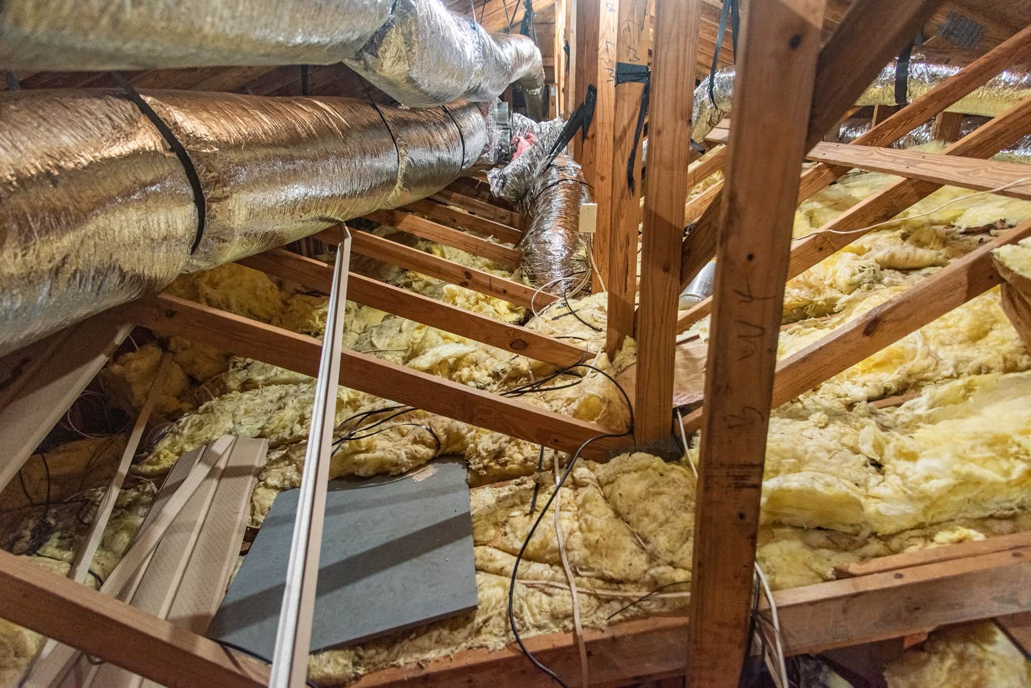 Fiberglass batts thrown over ducts and wiring in an attic, gaps everywhere
